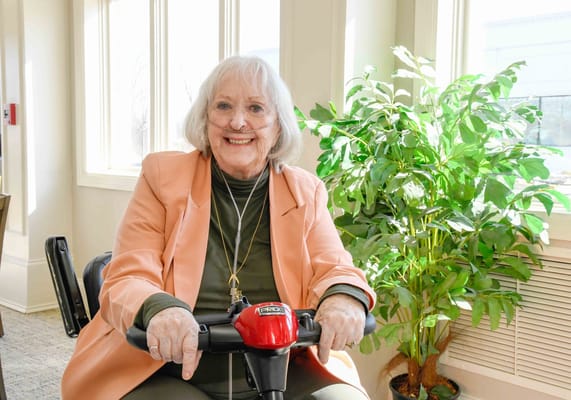 Smiling resident on mobility scooter in a bright room