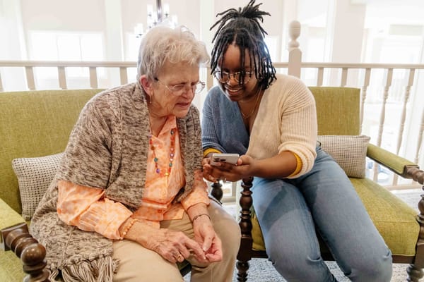 Resident and staff member engaging with a phone in a cozy seating area