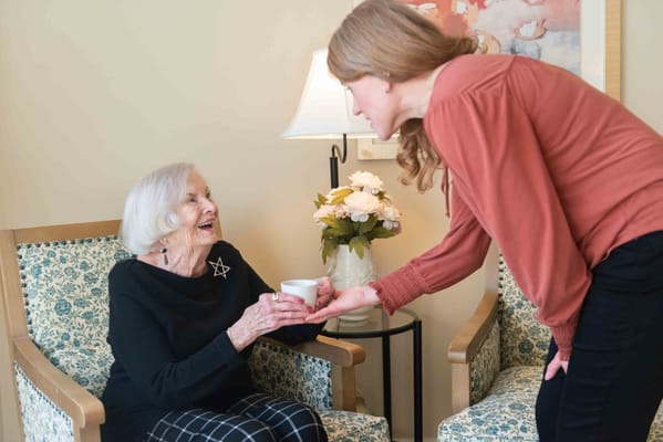 Staff member serving tea to a smiling resident in a cozy setting