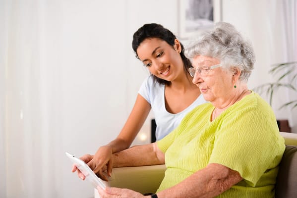 A caregiver assisting a senior woman with a tablet