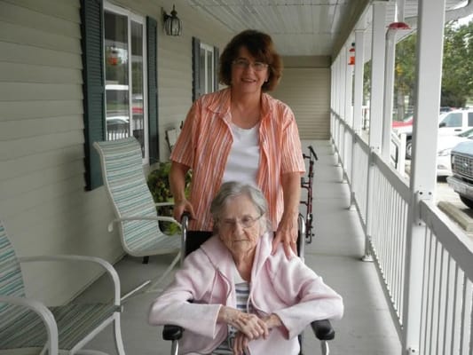 A caregiver assisting an elderly resident on a porch