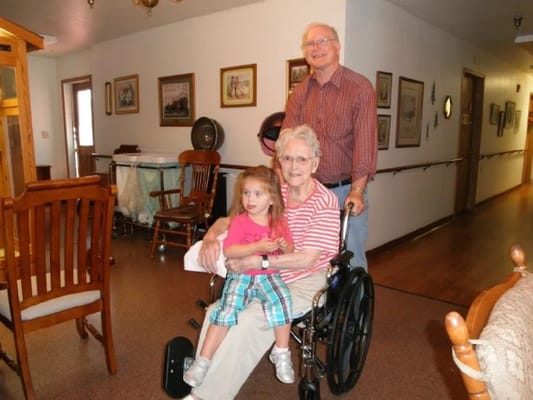 A resident in a wheelchair with a child and family member in a hallway