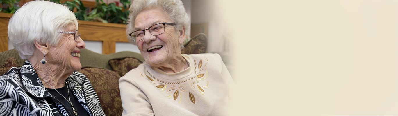 Two elderly women laughing together on a couch