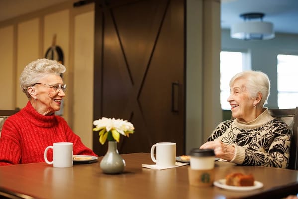 Two elderly women enjoying coffee and pastries at a table