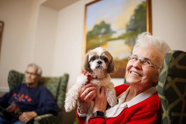 Senior resident smiling with a dog in the lobby