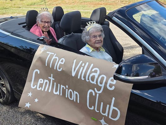 Two residents in a convertible with a celebration banner