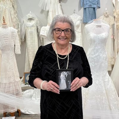 Senior woman holding a wedding photo surrounded by dresses