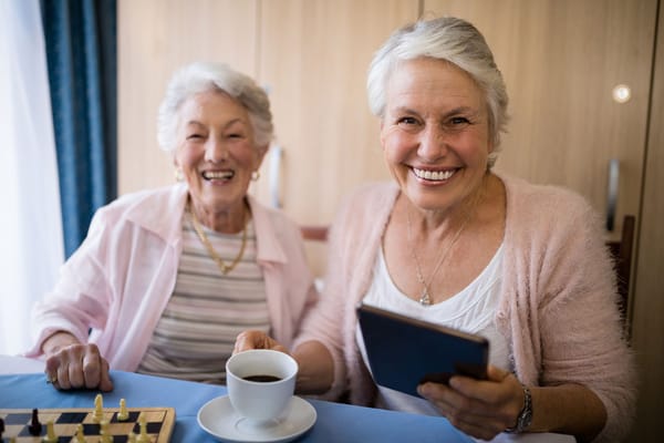 Two smiling residents enjoying coffee and playing chess