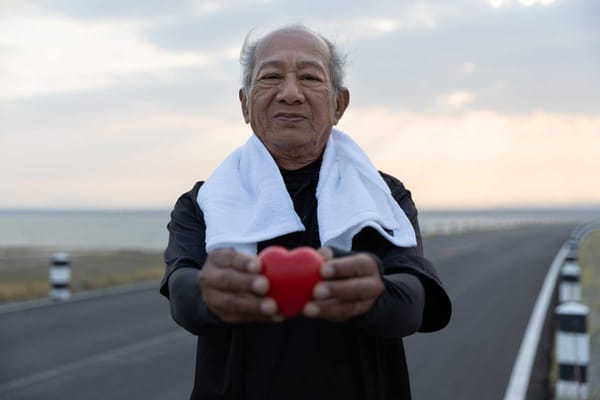 Elderly man holding a heart on a quiet road