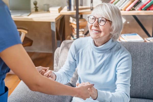 A caregiver interacts with a smiling elderly resident