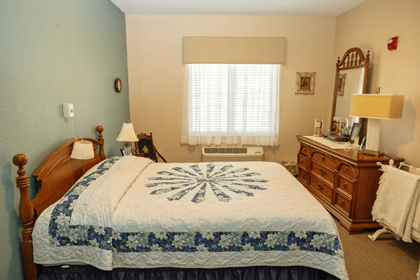 A cozy resident room with a decorated bed and dresser
