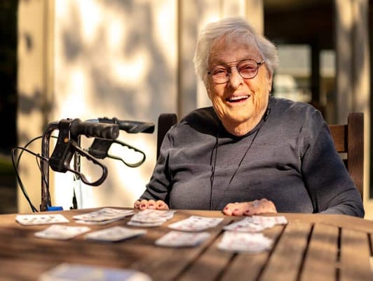 Senior resident smiling while playing cards outdoors