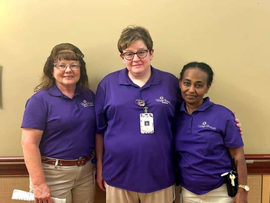 Three staff members in purple uniforms smiling together