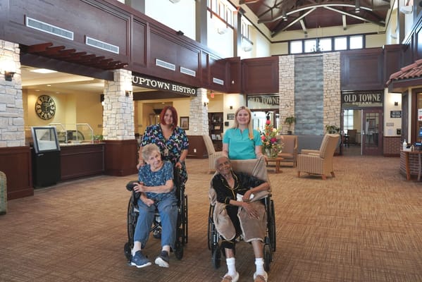 Residents in wheelchairs with staff in a welcoming lobby