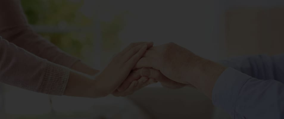 Hands of a caregiver and a senior resident holding each other