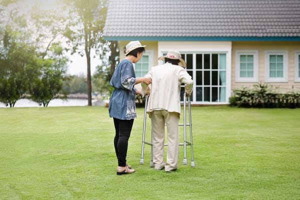 A resident using a walker with assistance in a garden