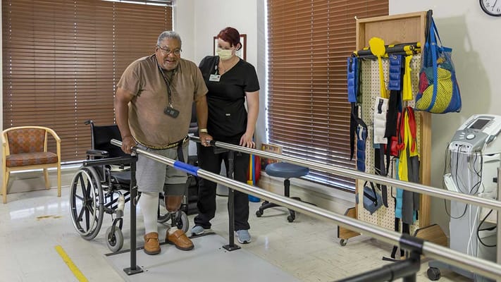 Resident practicing physical therapy with staff assistance
