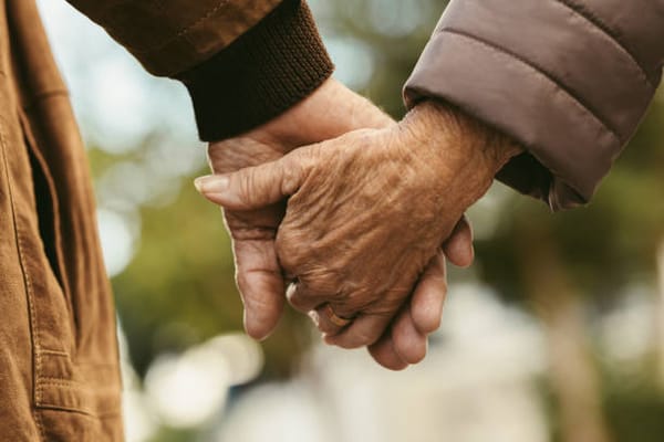 Two elderly hands holding each other outdoors