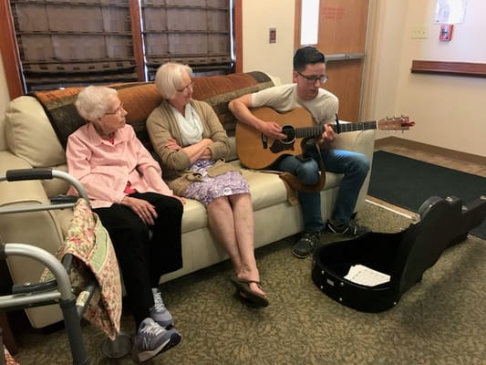 A musician playing guitar for two residents in a cozy setting
