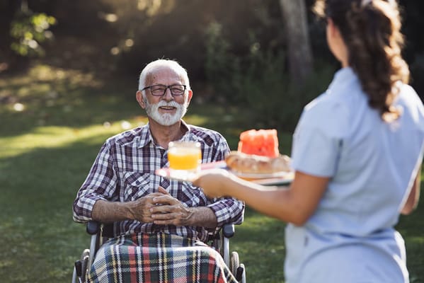 A caregiver serving food to a smiling resident in a garden