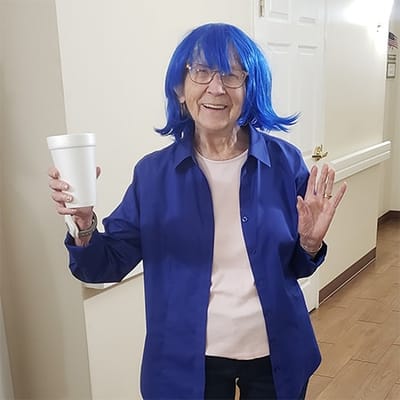 Resident with blue wig holding a drink in the hallway