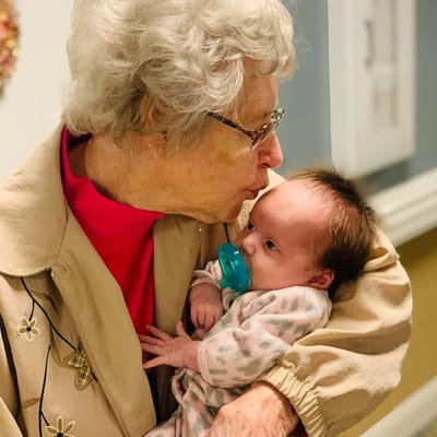 An elderly woman kissing a baby on the forehead