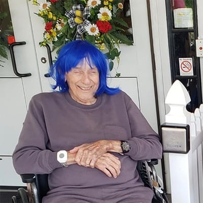 Resident with blue wig smiling outside the facility