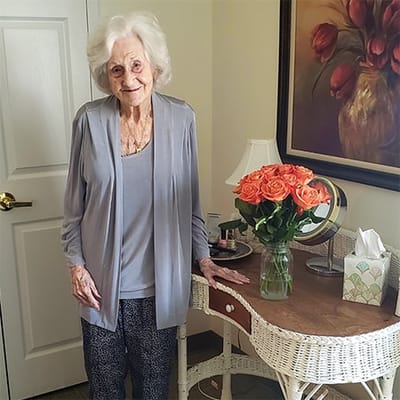 A resident smiling in her interior room with flowers