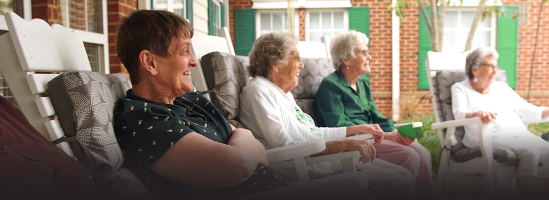 Residents enjoying a sunny day in rocking chairs on a porch