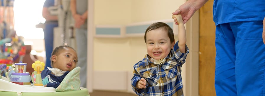 A child walking in a facility's interior with staff assistance