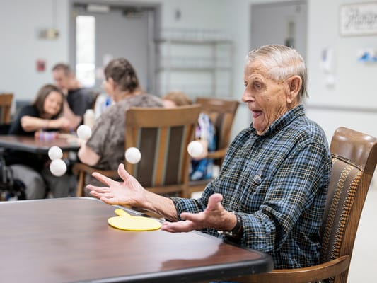 An elderly man joyfully playing a game with balls indoors