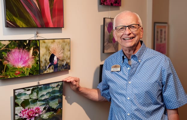 A resident smiling next to framed flower photos in a common area