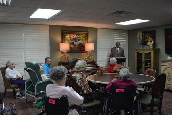 Residents and staff in an activity room listening to a speaker