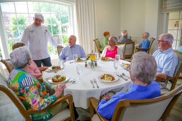 Residents enjoying dinner with a chef in a dining room
