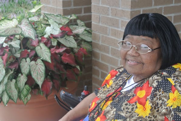 Elderly woman smiling by a potted plant in an outdoor setting