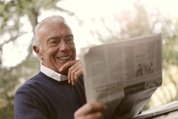 Smiling older man reading a newspaper outdoors