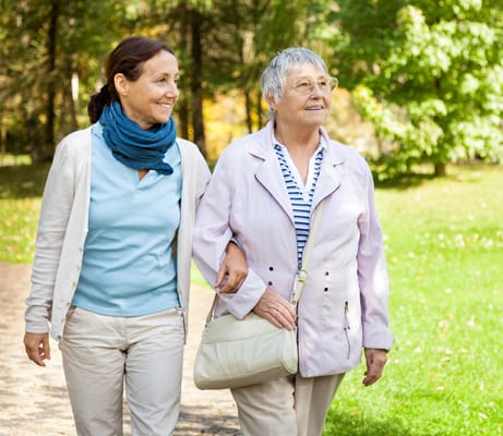 A caregiver walking with a senior woman in a park