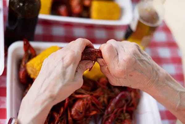 Elderly hands peeling crawfish and corn on a checkered tablecloth
