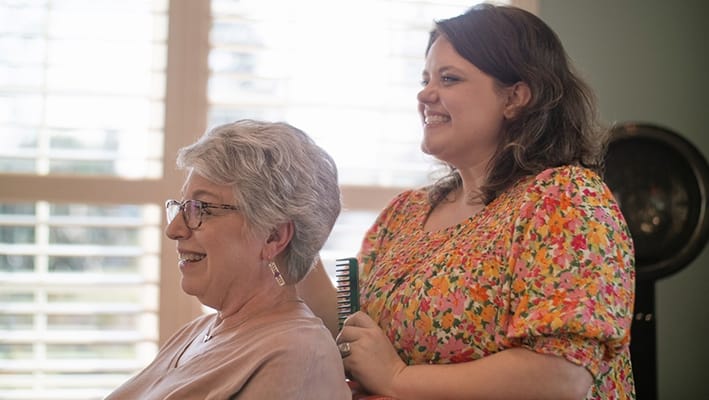 Staff member styling resident's hair in an interior space