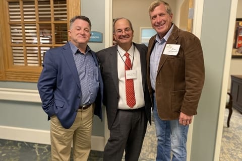 Three men in professional attire posing in a hallway