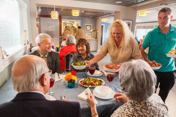 Residents enjoying a meal in the dining room with staff service