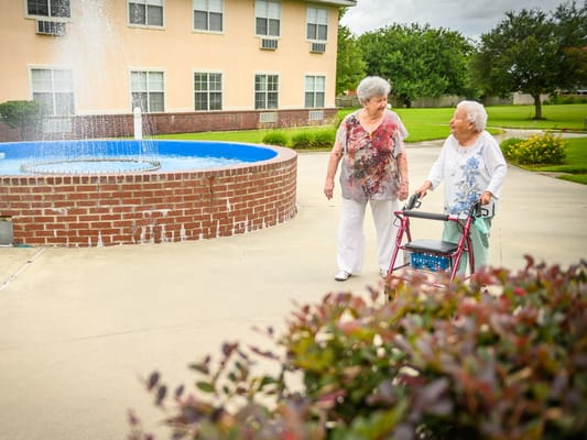 Two senior residents walking near a fountain in the garden