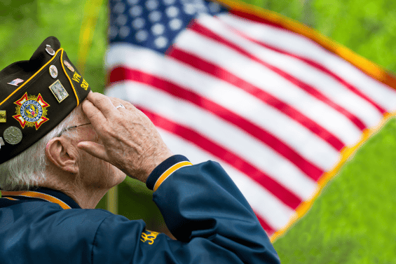 An elderly veteran saluting in front of an American flag