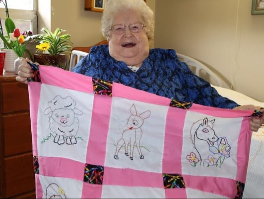 Resident proudly displaying a handmade quilt in her room