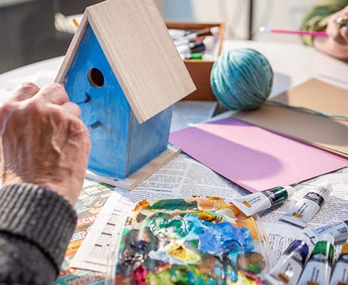 Close-up of hands painting a birdhouse during an activity