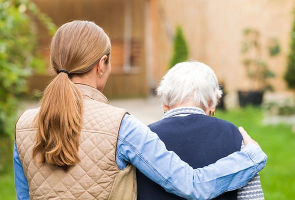 A caregiver walking with an elderly resident in a garden