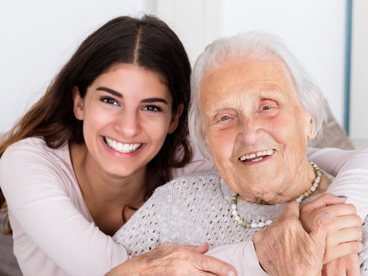 A smiling caregiver hugging a smiling elderly woman