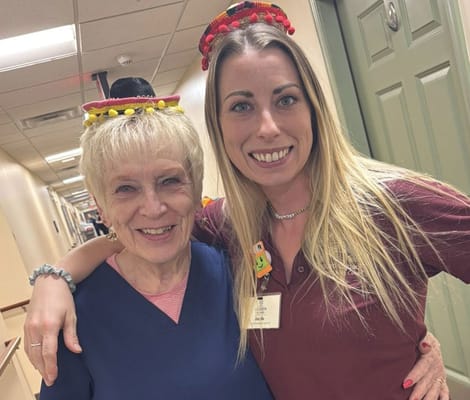 Staff member and resident wearing festive hats in the hallway