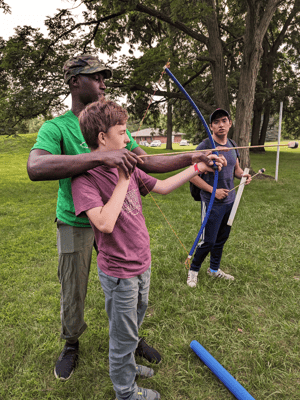 Two youths practice archery outdoors with an instructor