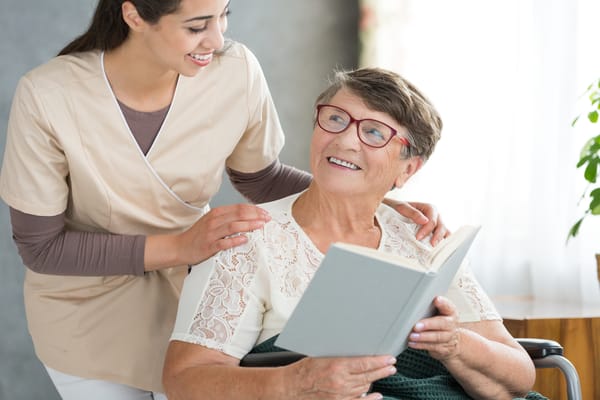 Caregiver assisting a smiling resident reading a book